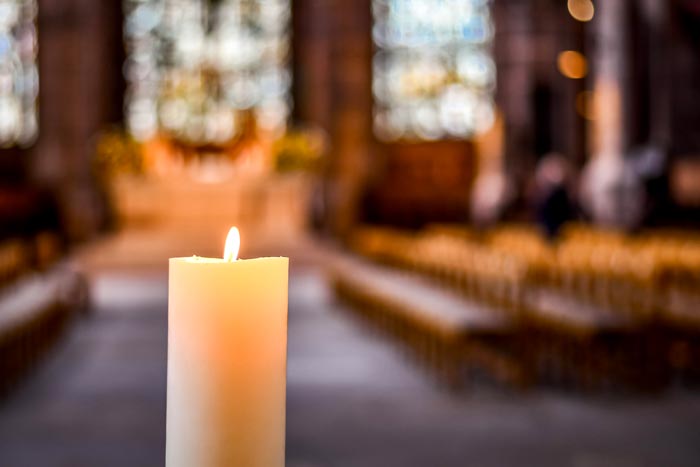 Närbild av ett vitt levande ljus som brinner med en klar, lugn flamma i en kyrka