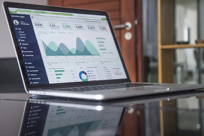 Två kvinnliga dataanalytiker som arbetar tillsammans vid en bärbar dator som visar en dataanalys med olika grafer, diagram och finansiella visualiseringar