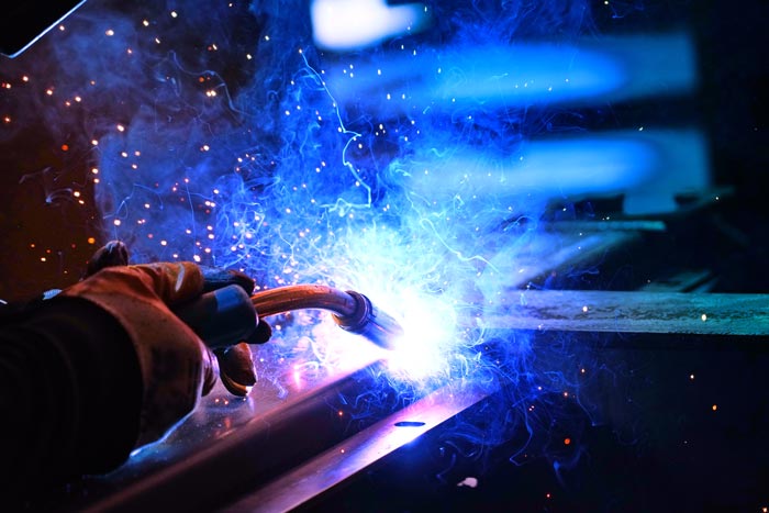 n svetsare utför metallsvetsning i sin verkstad där intensiva blå gnistor sprutar från svetspunkten