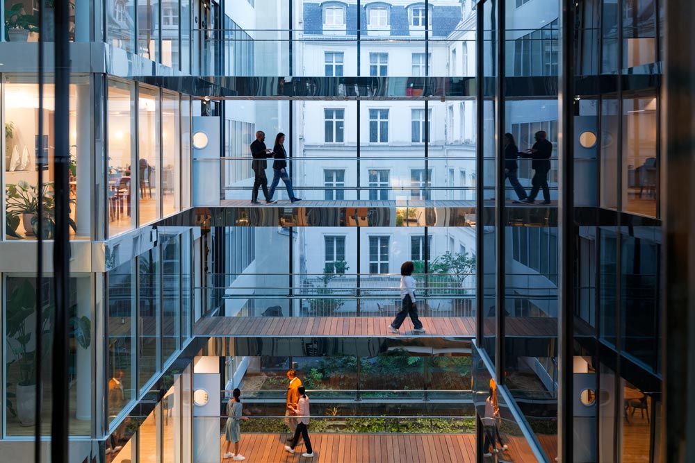 En modern kontorsbyggnad i Paris med glasväggar där silhuetter av affärskvinnor och affärsmän korsar upphöjda gångbroar på flera nivåer
